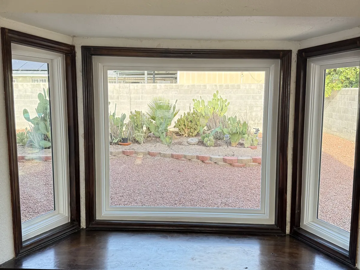 Bay window seen from inside, dark wood surround and seat, looking out to desert landscaping.