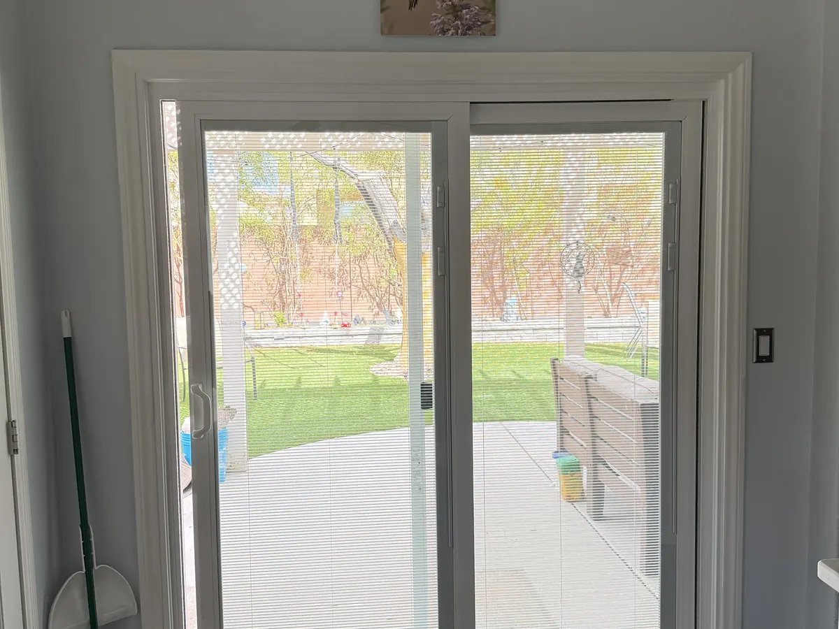 White sliding patio door with screen, seen from inside, opening onto a lawn.